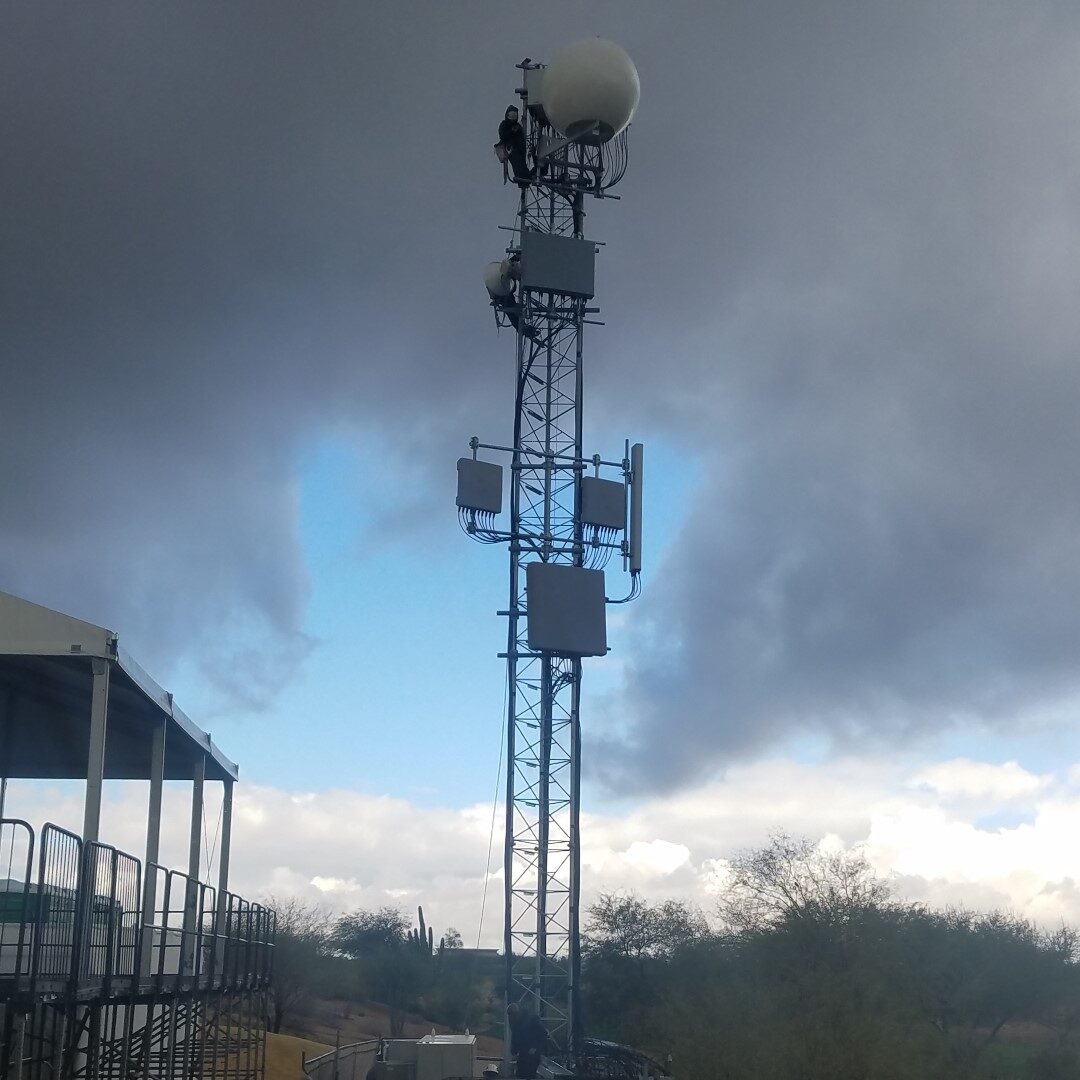 Crew on a temporary event tower with radome and panel antennas beside grandstand structure