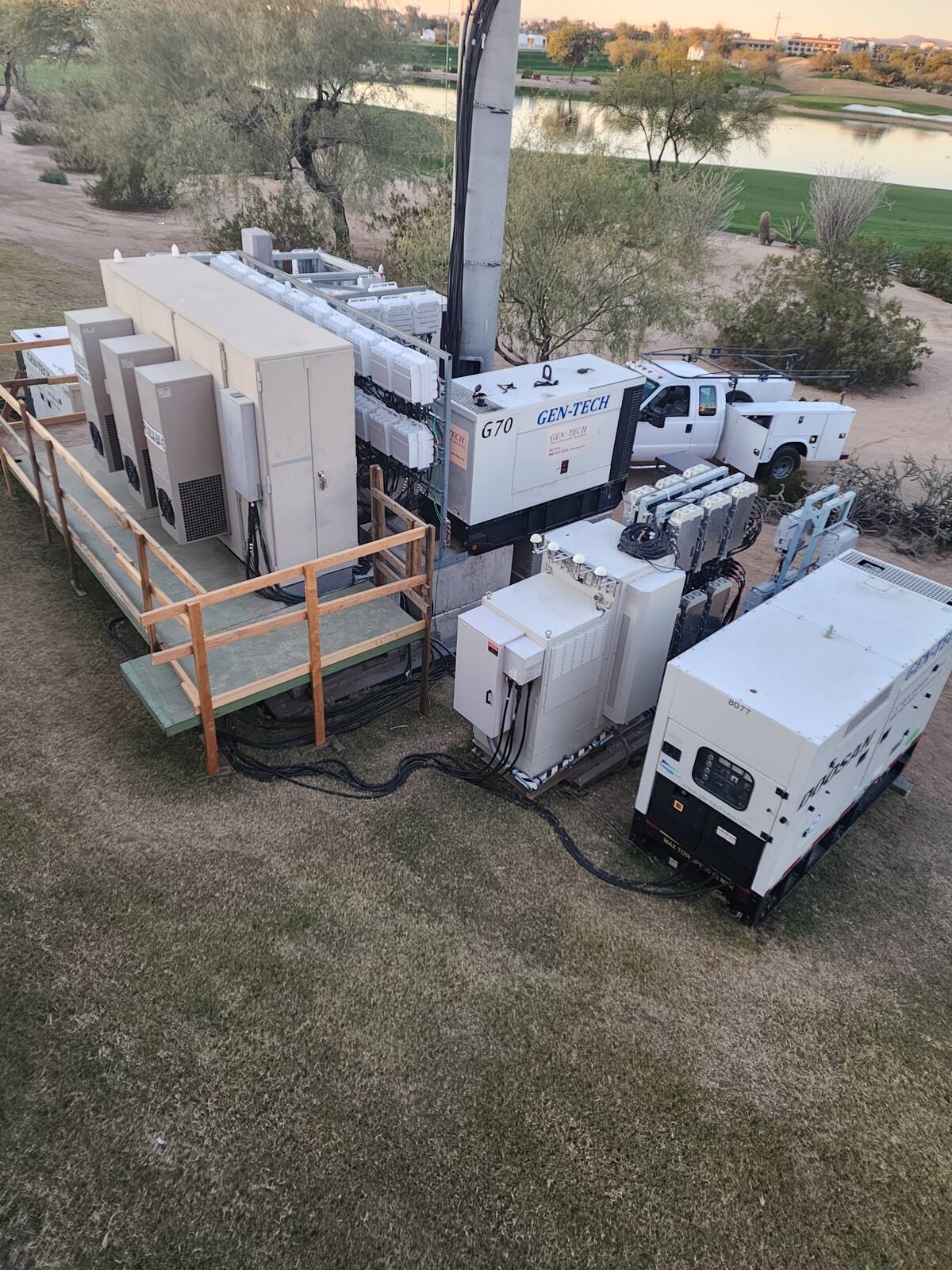 Temporary site power compound with generators and equipment cabinets beside a golf course