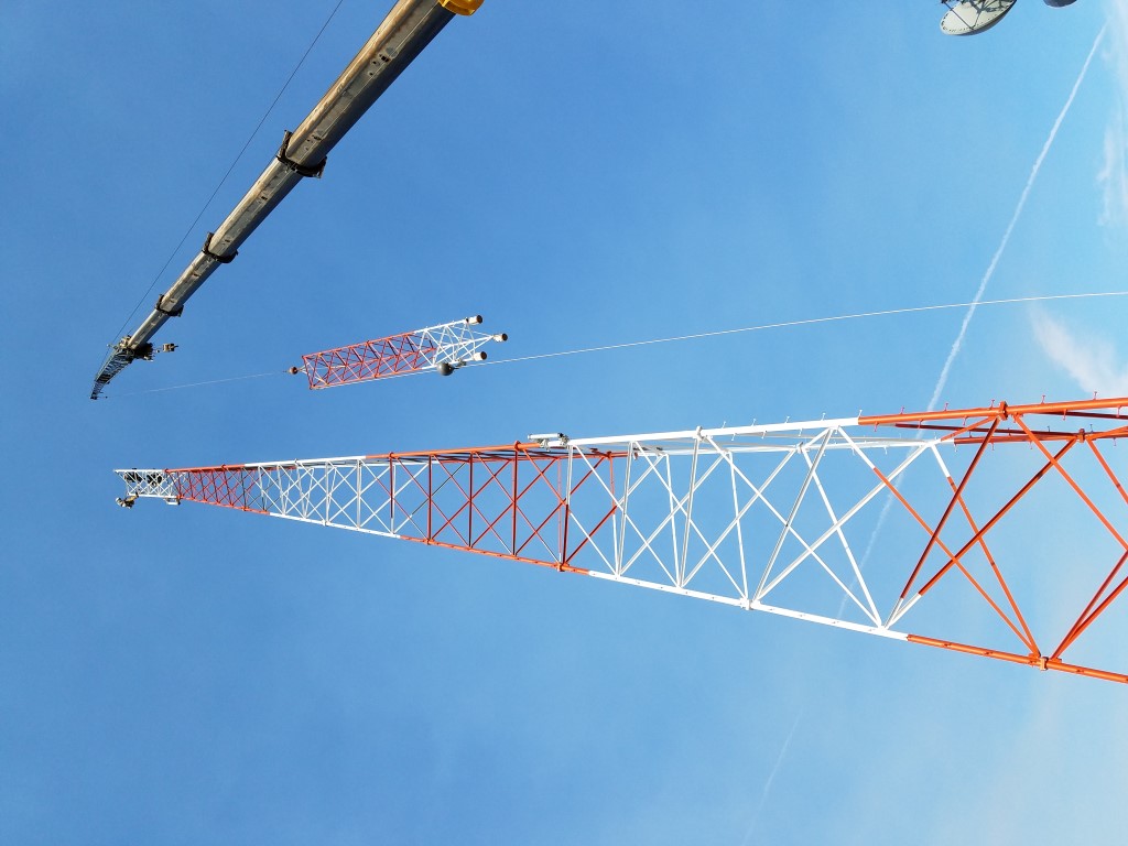 Crane setting a tower section beside a standing lattice tower